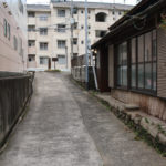 街道の先に車道と石碑と案内板がみえる(田中町-宿町)