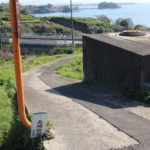 左下に街道の道標。実際の街道は左だが、現在の旅人はこの道を行く人が多い。奥の海に「鹿ノ島」がみえるが、その付近に旧街道が通っており、街道そのものも映っているが、遠すぎて分かりづらい。(東彼杵町里郷557付近)