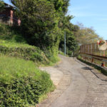 街道。道の先に街道の道標がある。右のフェンスの下は崖で、国道と線路と海(瀬戸郷1331付近)